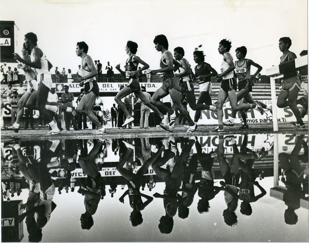 Atletas y su reflejo en el agua. Una bella imagen que juega composicionalmente con los atletas y sus reflejos en el agua. Con esta fotografía Caicedo logra resaltar el aspecto más plástico de este deporte al tiempo que realiza un guiño a la historia misma de la fotografía y los referentes modernistas que tanto influyeron en su práctica.