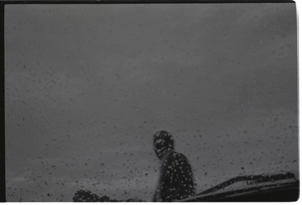 Esta imagen es una captura misteriosa del agua sobre un vidrio de un carro en contraste con la silueta de un hombre mojándose.