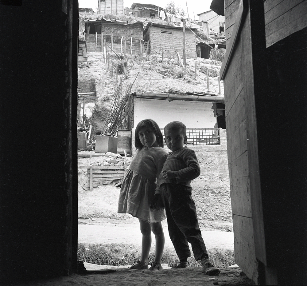 Barrio Egipto, Bogotá, 1955. Negativo de 6x6 cm. Una evidente preocupación social marcó gran parte del trabajo fotográfico de Caicedo, particularmente en relación a la fotografía de niños en entornos urbanos precarios. Esta imagen es una muestra de este interés y de la forma muy acertada en la que se emplea el marco de una vivienda humilde para sugerir la imposible separación entre hogar y calle como duro hábitat de estos niños.