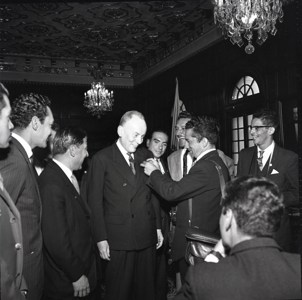 Alberto Lleras Camargo y posiblemente reporteros gráficos en la Casa de Nariño. Lleras Camargo recibe una condecoración. Foto tomada en la Casa de Nariño, durante su segundo mandato como presidente de Colombia, entre 1958 y 1962. Esta época se le conoce en política como el Frente Nacional.